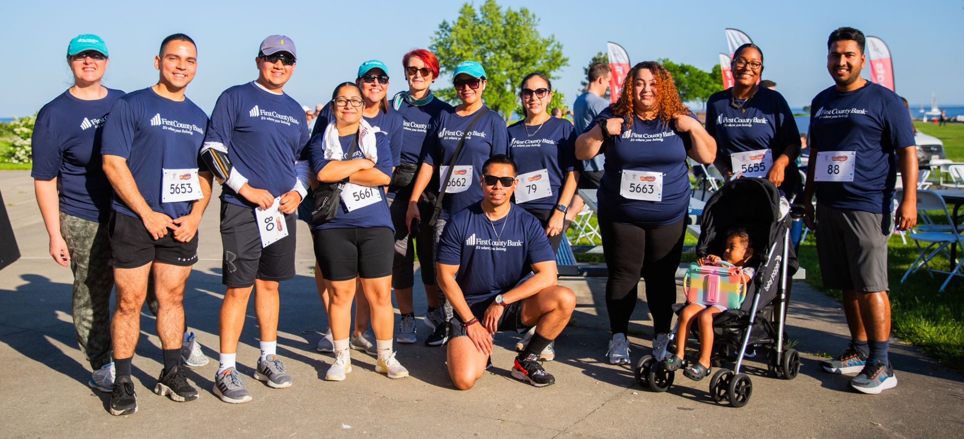 First County Bank staff in navy branded shirts with race bibs, at a community road race on the Stamford waterfront